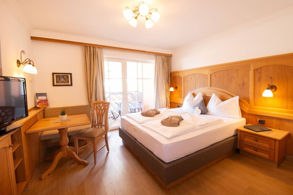 A hotel room with a bed, a desk, a chair, a television, and a window with curtains.