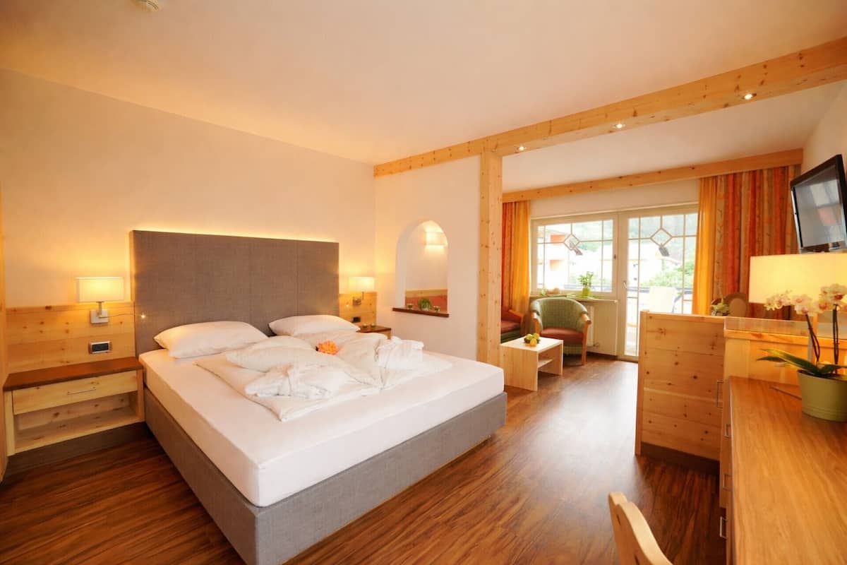 A hotel room with a bed, bedside tables, a desk, a chair, and a television.