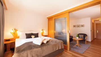 Une chambre d’hôtel avec un grand lit, des lampes de chevet, une petite table avec une plante et un canapé dans le salon attenant.
