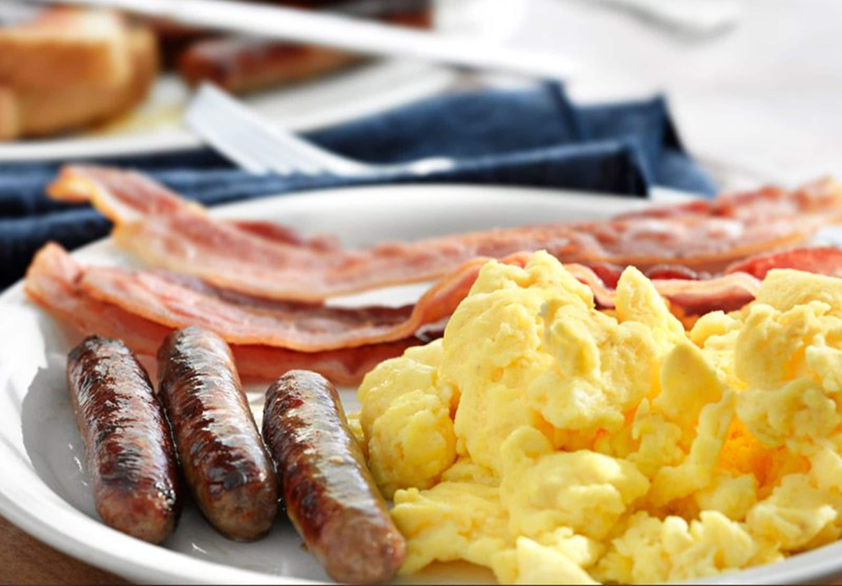 A plate with scrambled eggs, bacon, and sausages.