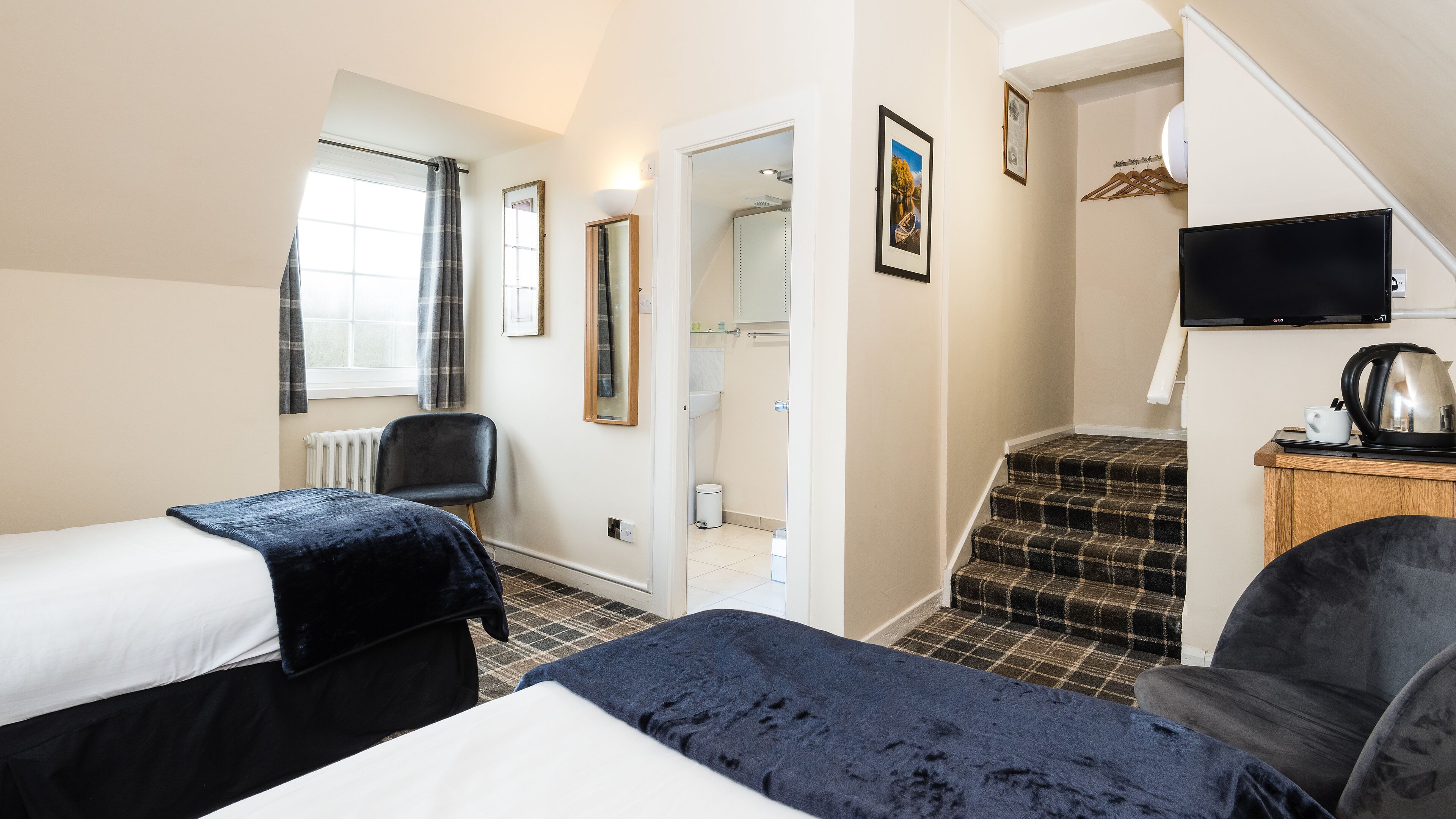 Ein Hotelzimmer mit zwei Betten, einem Sessel, einem Fernseher und einer Treppe, die ins Badezimmer führt.