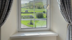 Ein Fenster mit Blick auf eine grüne Landschaft, Vorhänge und ein weißer Fensterbrett.