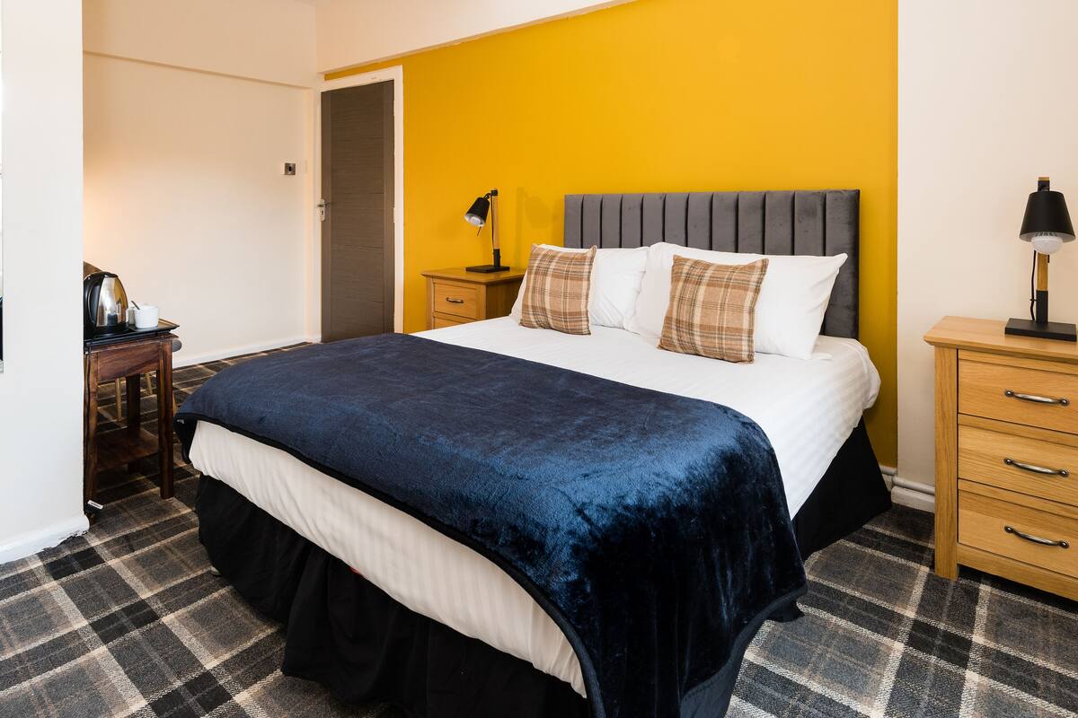 Ein Hotelzimmer mit einem Bett, einem Nachttisch, einer Lampe und einer Holzkommode.