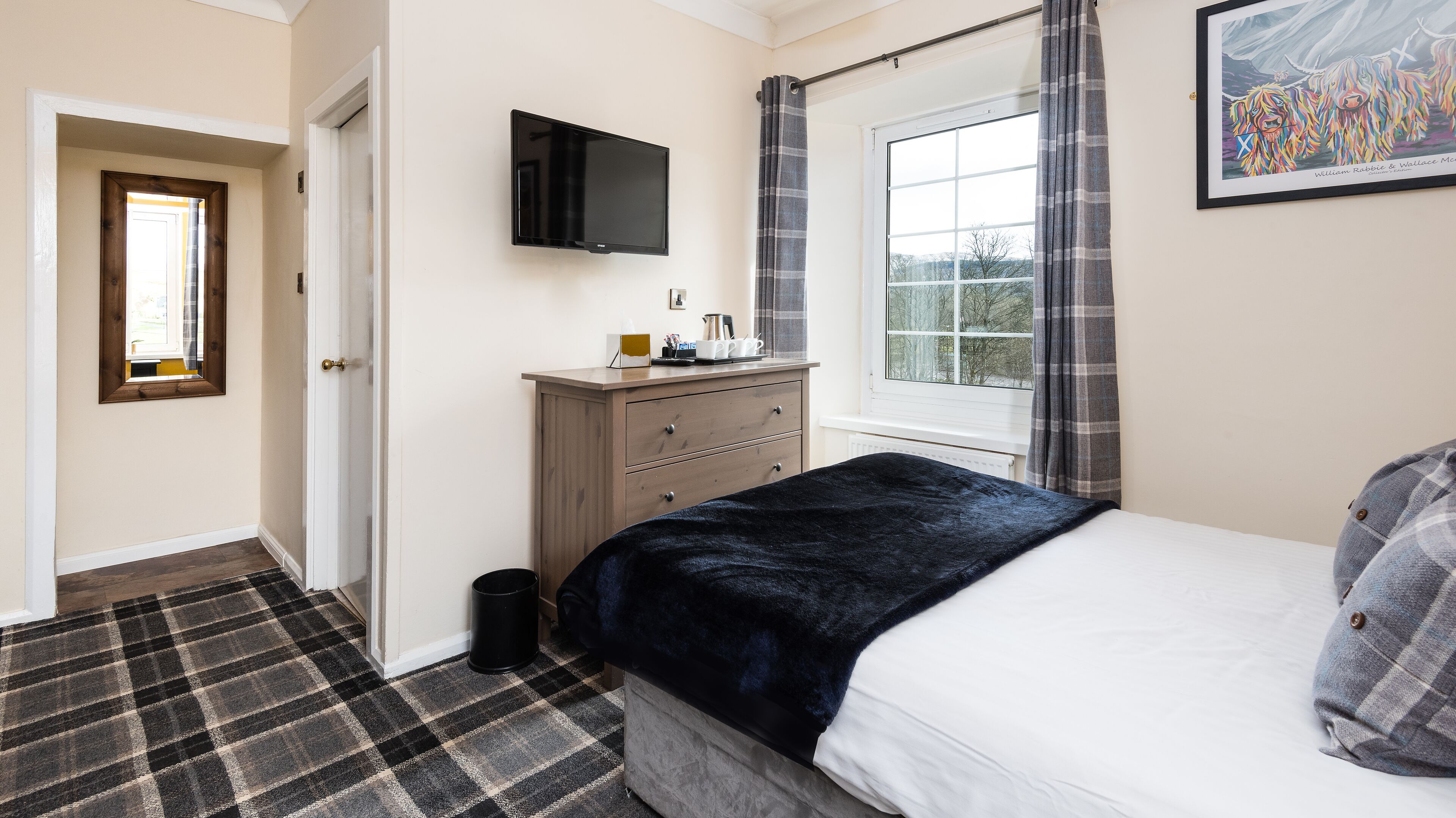 Une chambre à coucher avec un lit, une commode, un téléviseur et une fenêtre avec des rideaux.