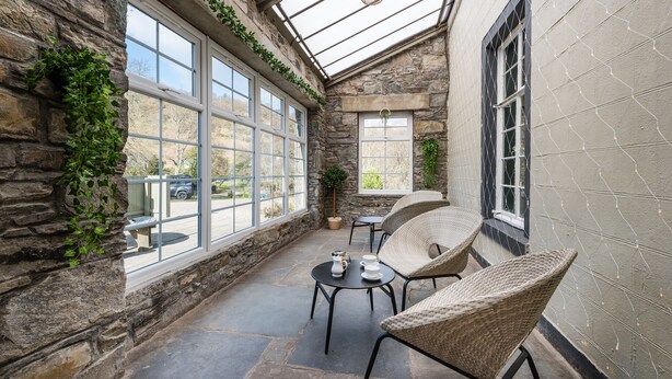 Eine gemütliche Terrasse mit Steinmauern, großen Fenstern, Korbstühlen und einem Tisch mit Teeservice.