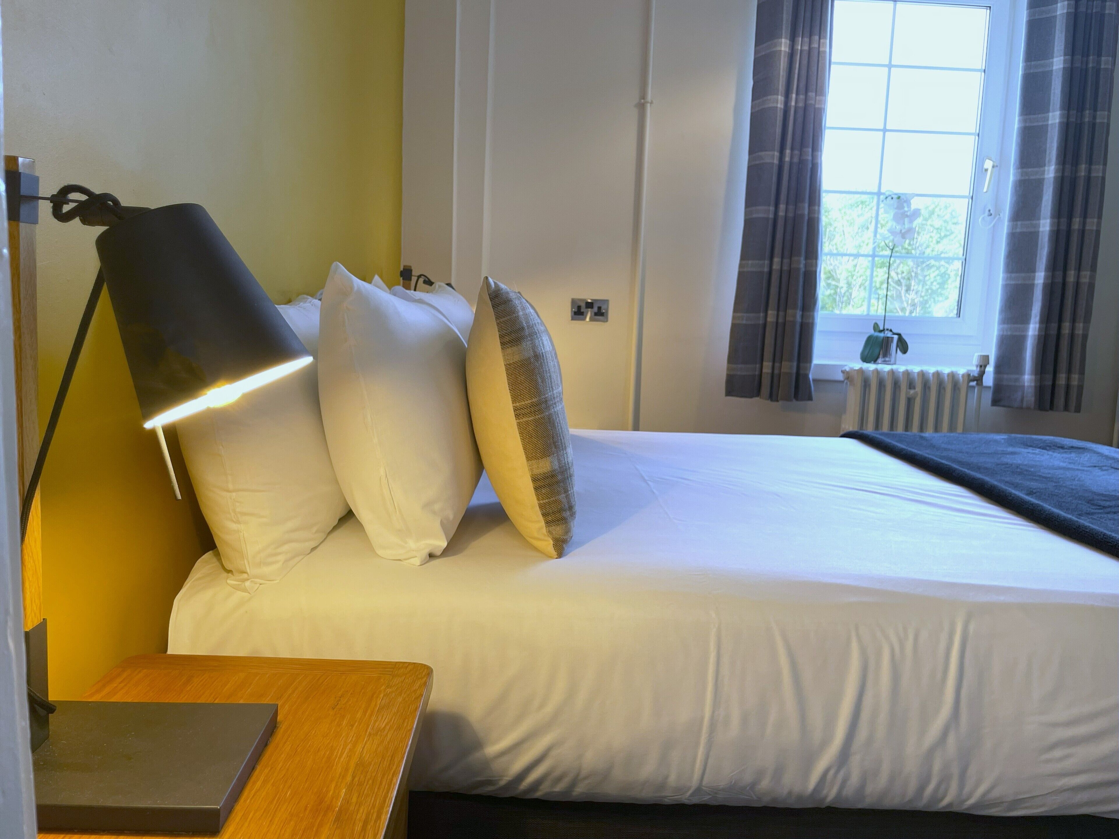 Una cama bien tendida con sábanas blancas, una lámpara de noche y una mesita de madera.
