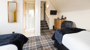 Un dormitorio con dos camas, un aparador, una silla, un televisor y una escalera que lleva a un baño.
