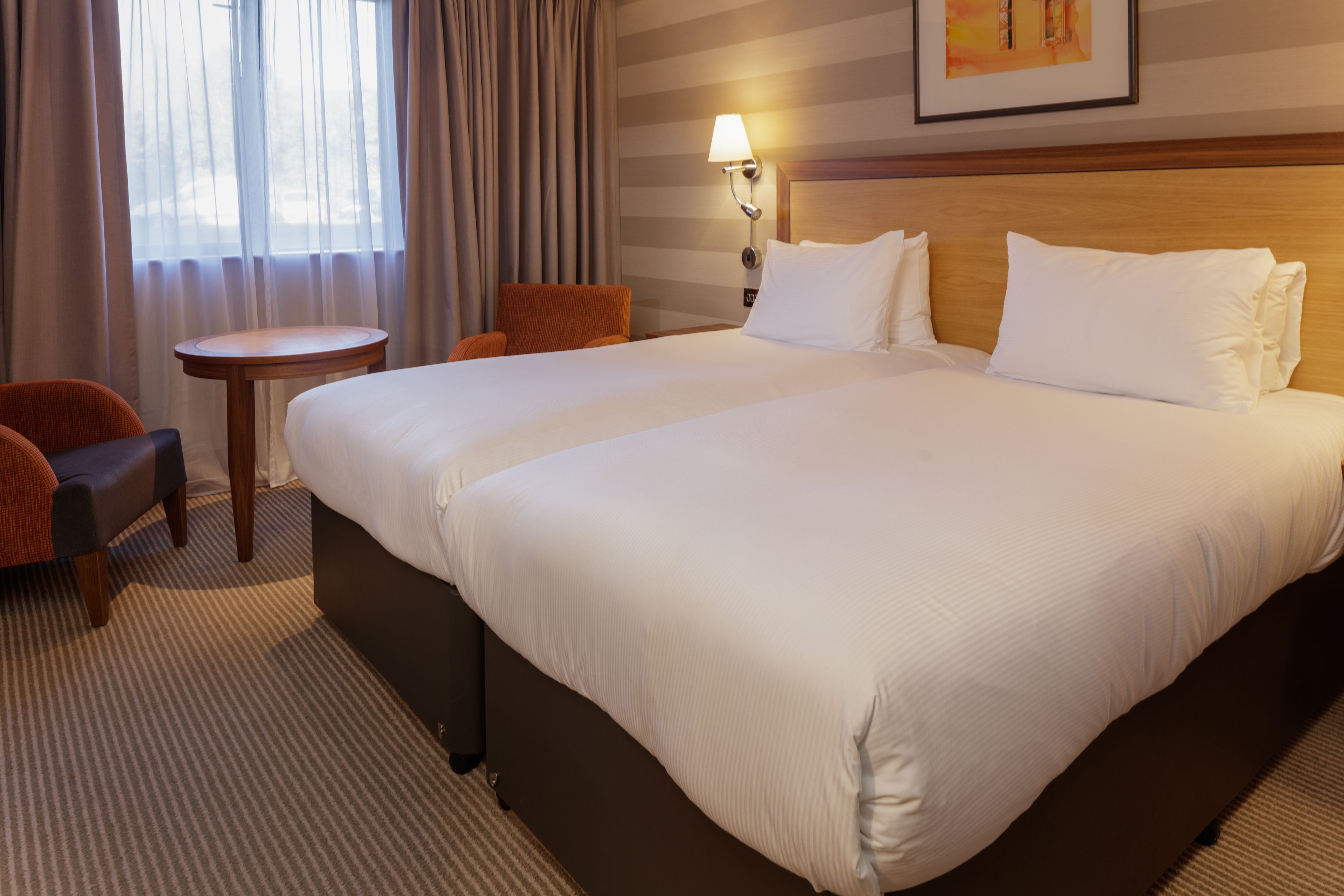 A hotel room with a large bed, a small table, a chair, and a lamp.