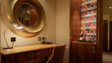 Une chambre d’hôtel avec un bureau en bois, un miroir rond, une lampe, un téléphone et un mur décoré de divers autocollants.