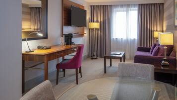 Une chambre d’hôtel équipée d’un bureau, d’une télévision, d’un canapé et d’une table en verre.