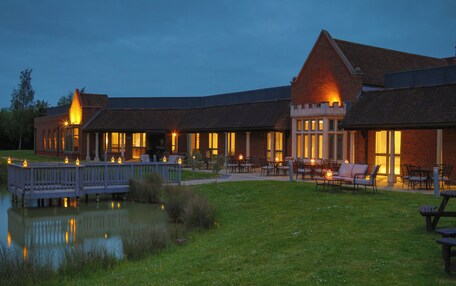 A building with a pond in front, outdoor seating, and a deck.