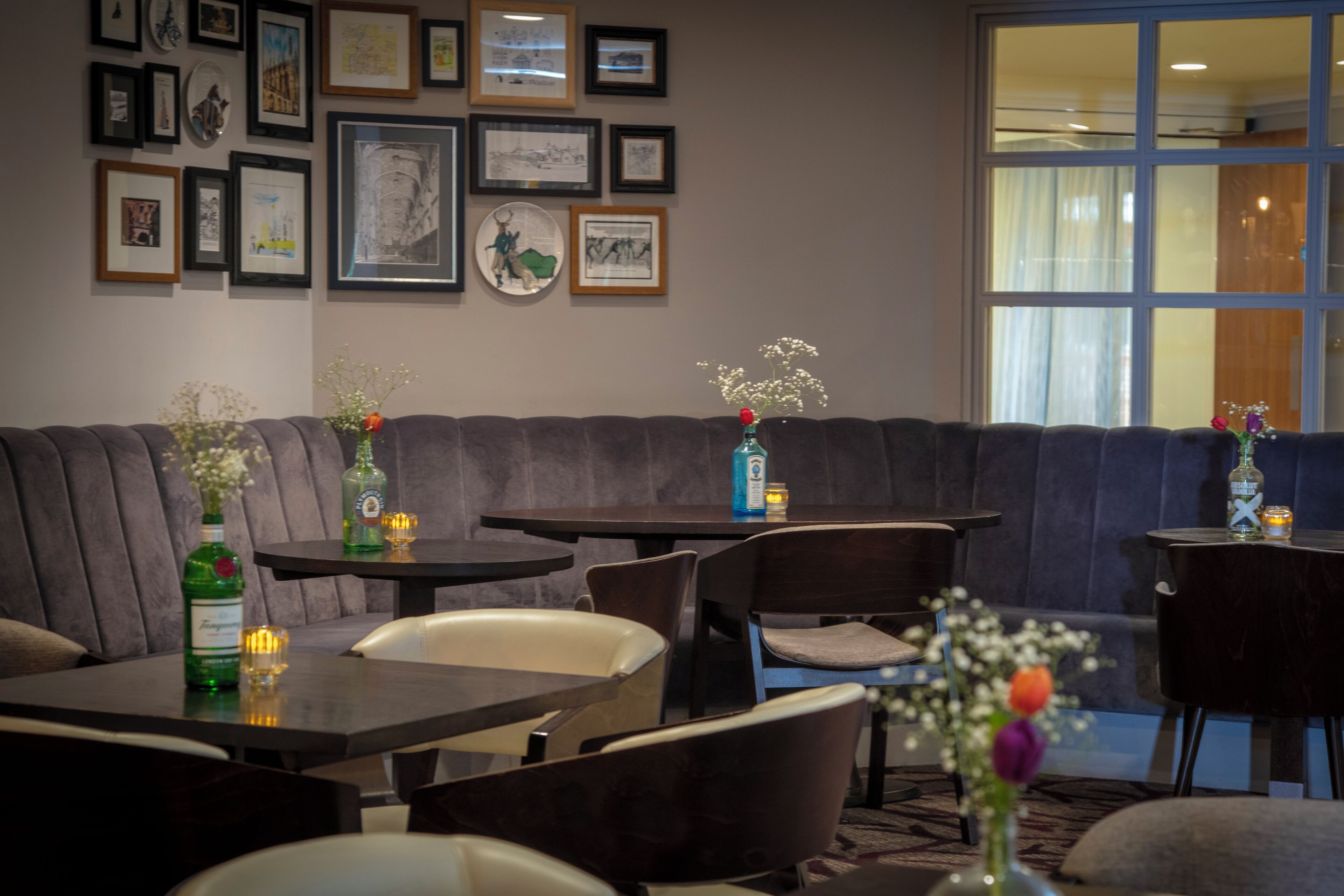 Eine Hotelhalle mit einem dunkelgrauen Sofa, mehreren Tischen, Stühlen und einer Wand mit gerahmten Kunstwerken.