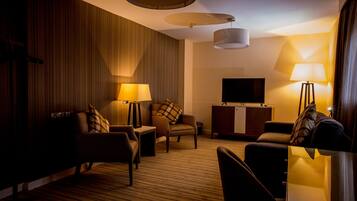 Una habitación de hotel con sofá, sillones, televisor y dos lámparas.