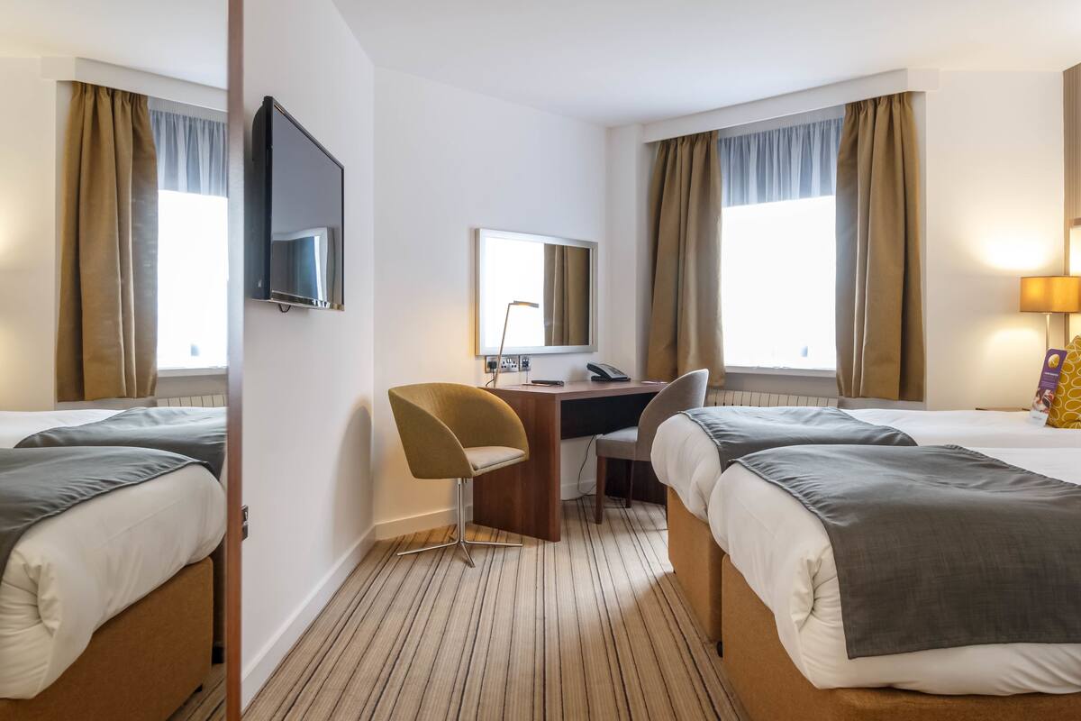 Habitación de hotel con dos camas, un escritorio, una silla, un televisor y una ventana con cortinas.