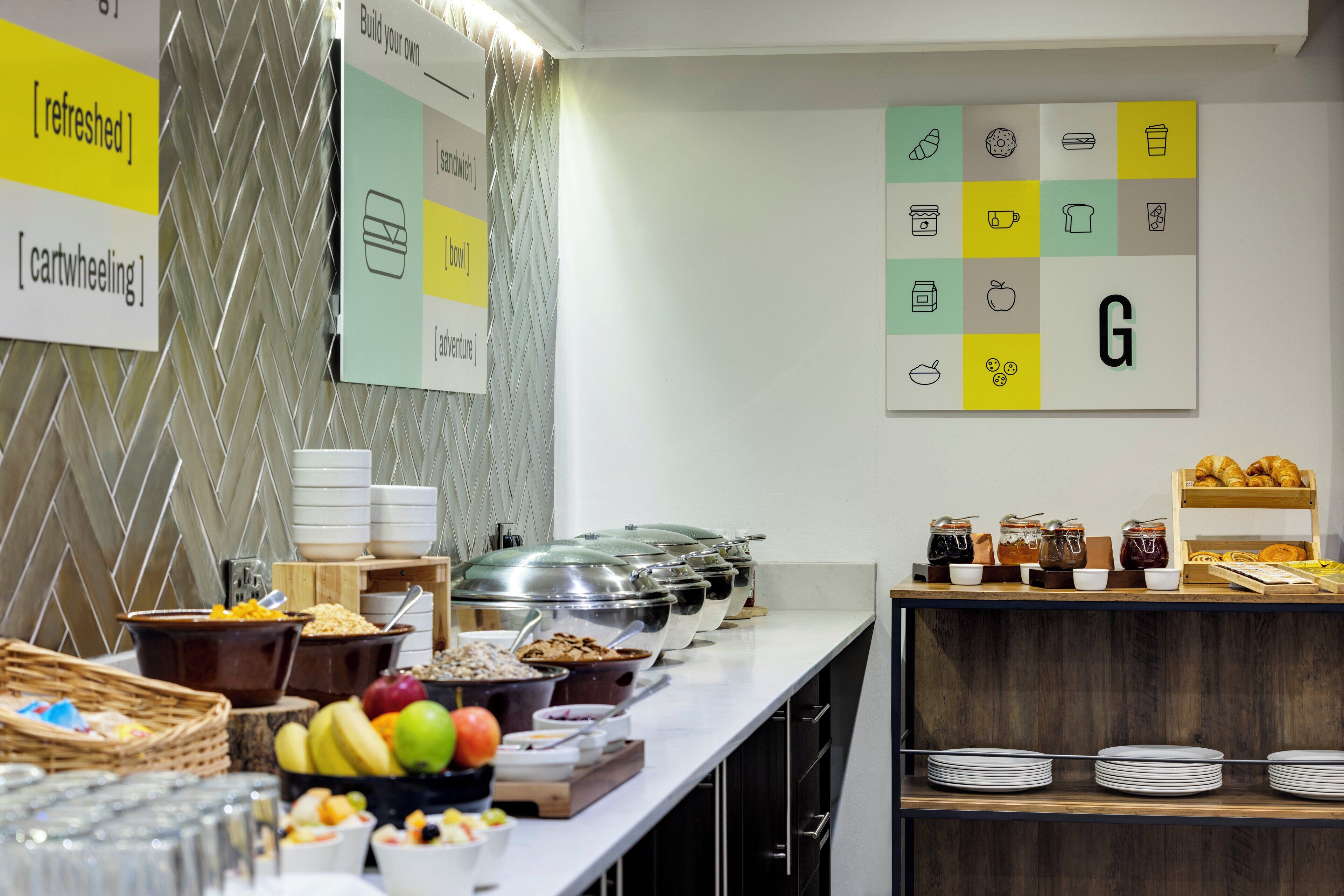 Montaje de buffet con diversos alimentos y recipientes, una pared con una cuadrícula de iconos de comida, y un letrero que dice 'cartwheeling'.