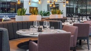 Un restaurant moderne avec des tables rondes disposées pour le service, agrémenté d’un arrangement floral central et d’un éclairage d’ambiance.