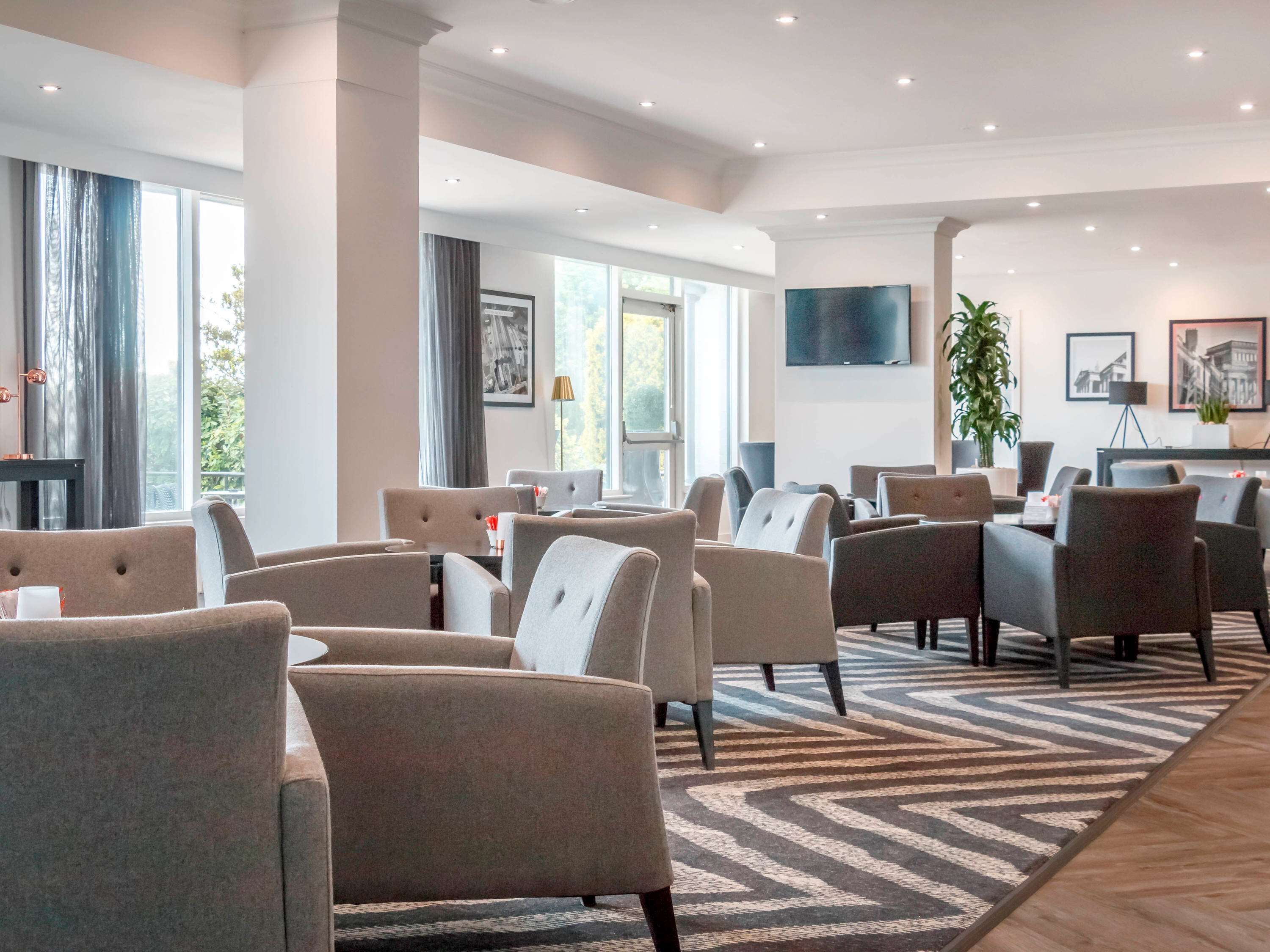 Un vestíbulo de hotel moderno con varias zonas de estar, un televisor grande y obras de arte en las paredes.