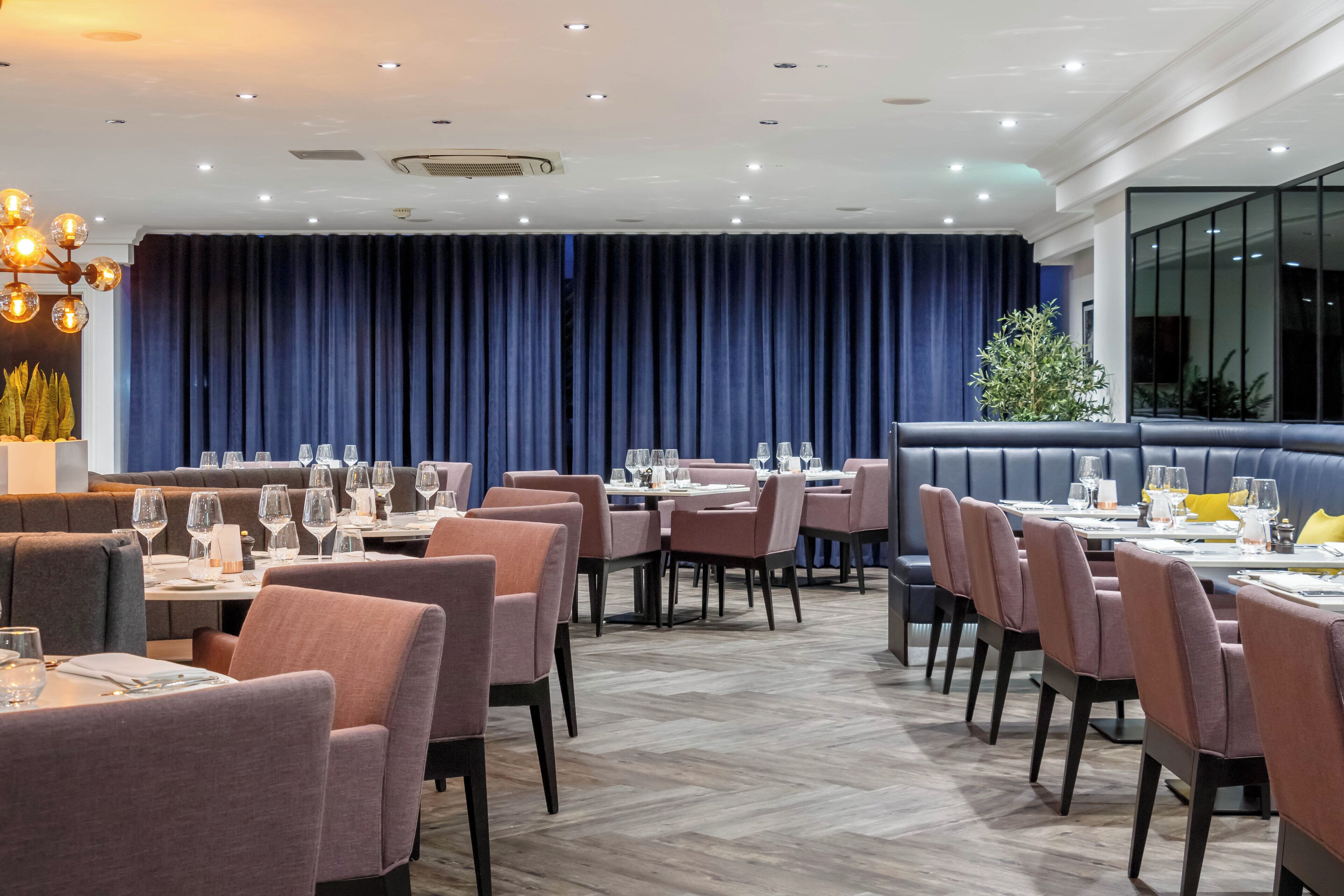 Un restaurant avec des banquettes et des tables, un fond en forme de rideau bleu et un lustre moderne.