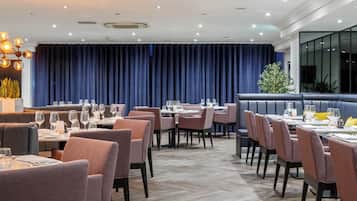 Un restaurant avec des banquettes et des tables, un fond en forme de rideau bleu et un lustre moderne.