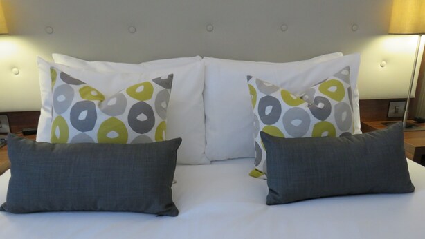Un lit doté d’une tête de lit capitonnée, de deux coussins décoratifs à motifs circulaires et de deux coussins unis de couleur grise.