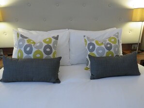 Una cama con cabecera capitonada, dos almohadas decorativas con diseño circular y dos almohadas grises lisas.
