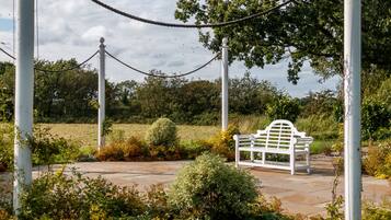 Un banc blanc dans un jardin, délimité par une barrière faite de cordes et agrémenté de colonnes blanches.