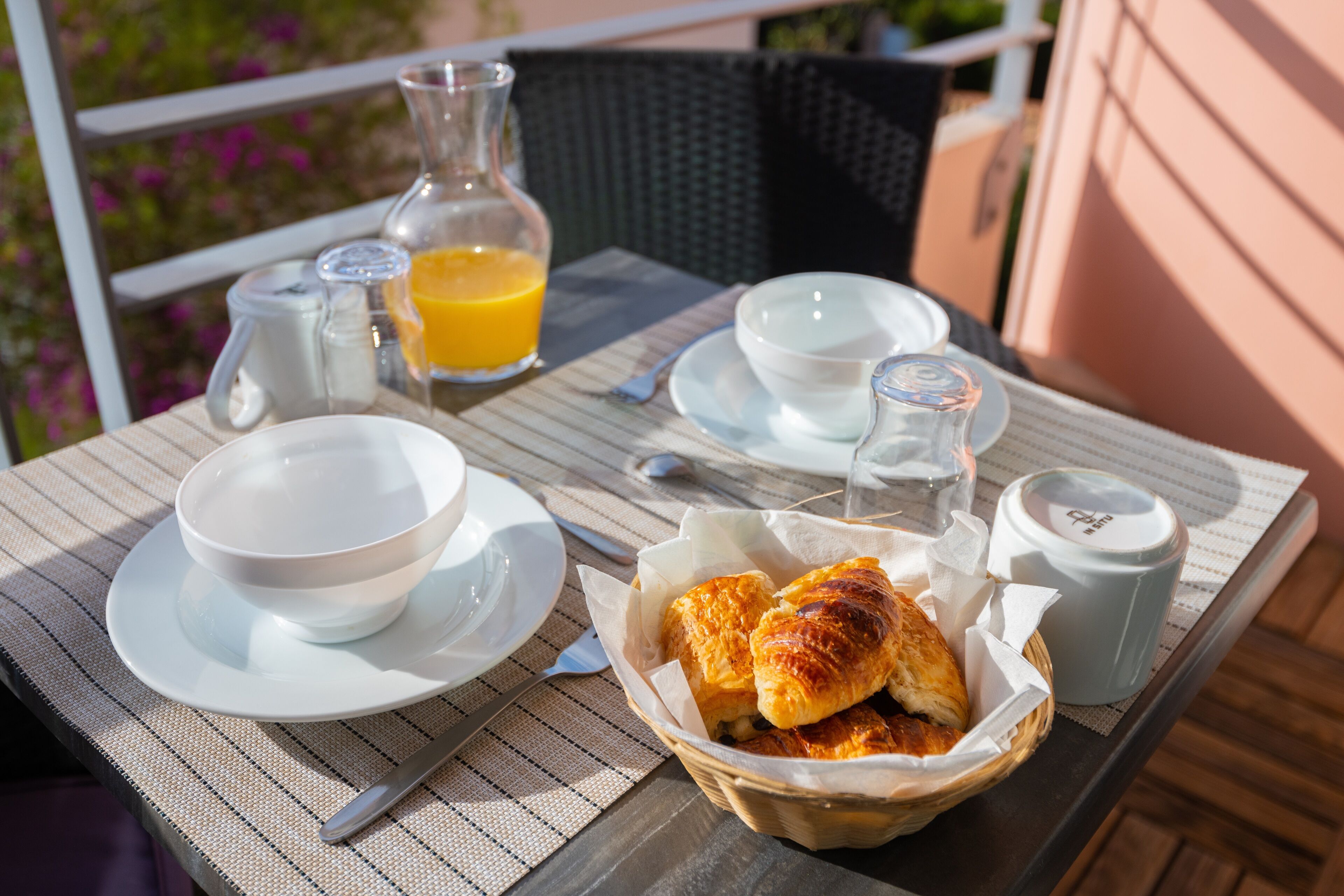 A table set for breakfast with a bowl, a cup, a jug, a bottle, and a basket of pastries.