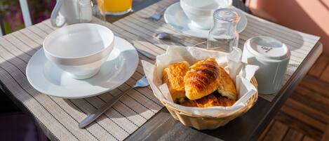 A table set for breakfast with a bowl, a cup, a jug, a bottle, and a basket of pastries.