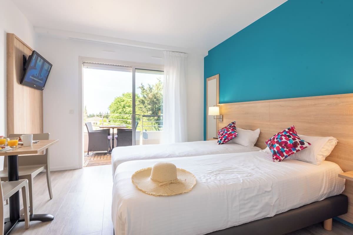 A hotel room with a large bed, a desk with a chair, a TV, and a balcony with outdoor seating.