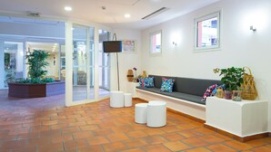 Un área de recepción con un sofá, taburetes blancos, una maceta con plantas y un televisor en la pared.