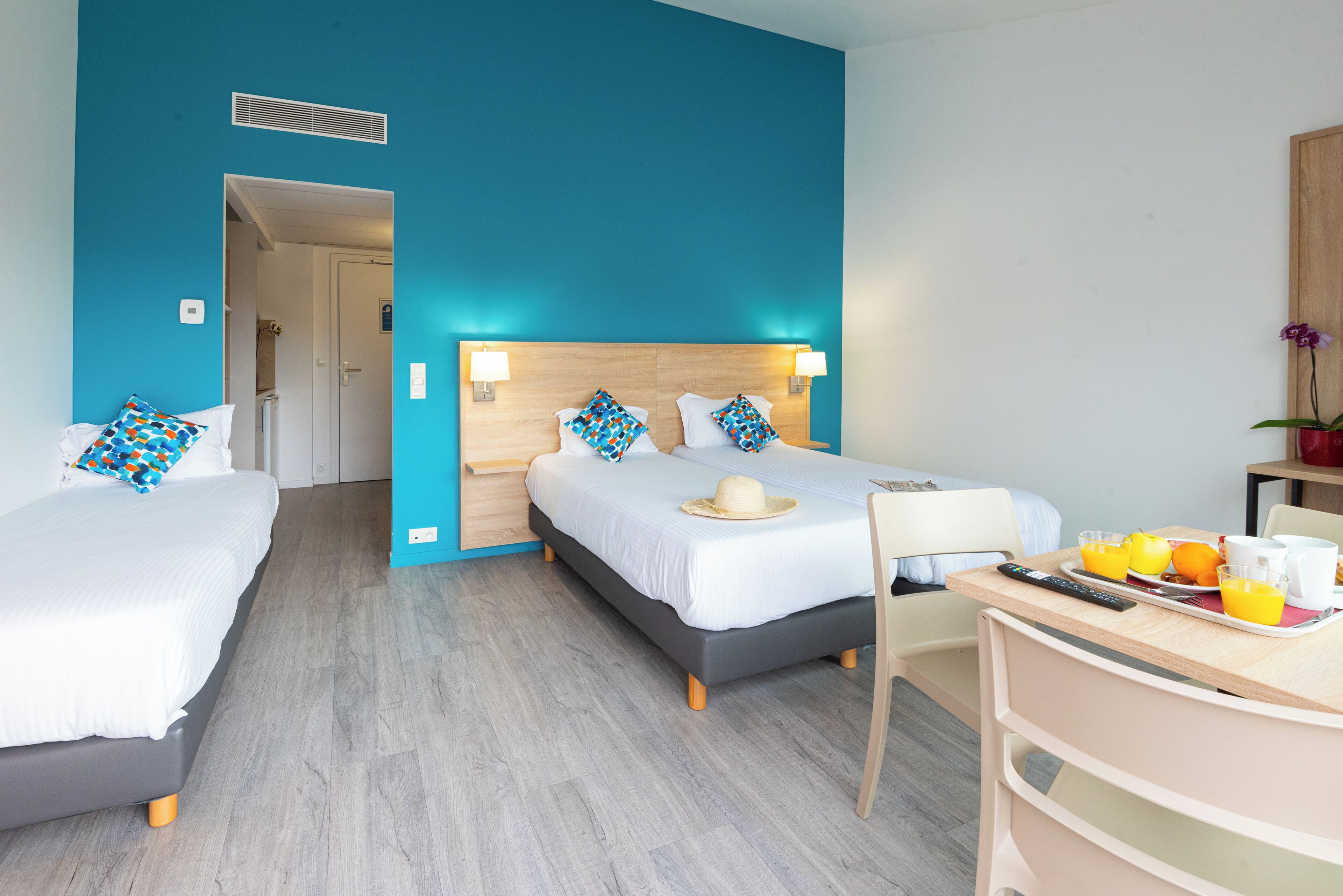 Habitación de hotel con dos camas, una mesa de comedor y alimentos para el desayuno, y una puerta de baño visible al fondo.