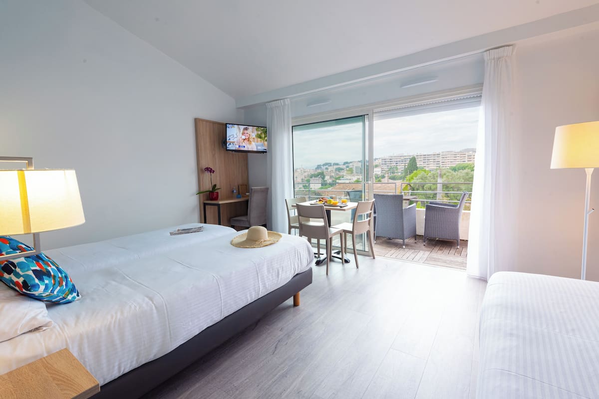 A hotel room with a bed, a desk, a TV, and a balcony with a view of the city.