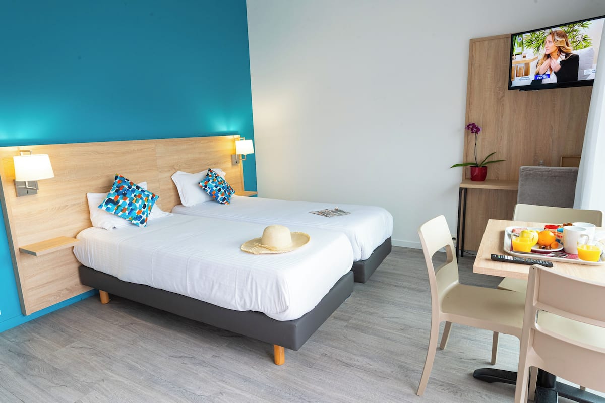 A hotel room with a bed, a desk with a chair, a television, and a small table with a plant and fruit.