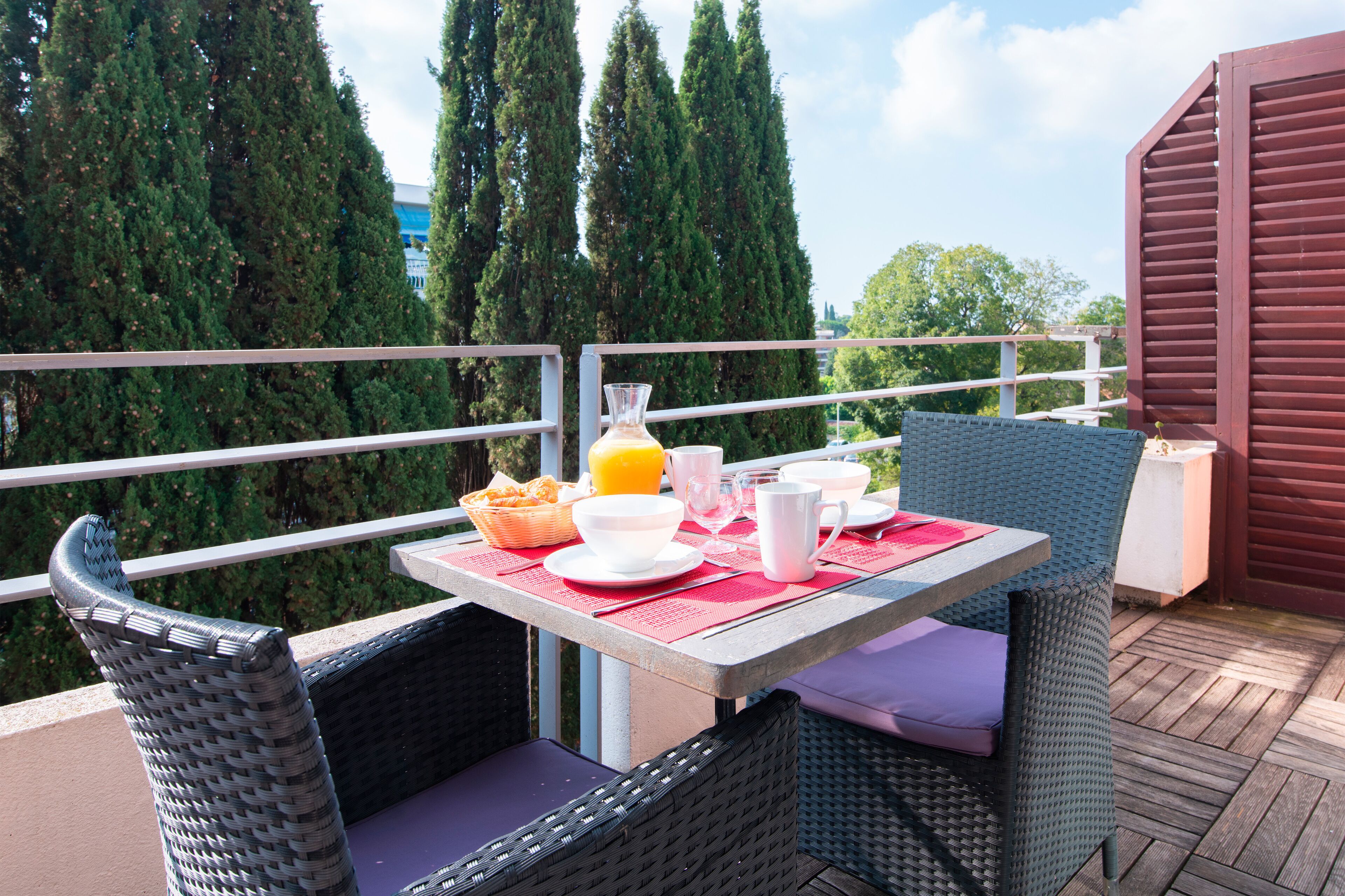 Een balkon met rieten stoelen en een tafel gedekt voor het ontbijt.
