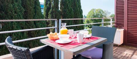 Een balkon met rieten stoelen en een tafel gedekt voor het ontbijt.