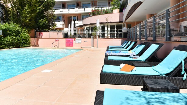 Zona de piscina con sillones de descanso y un edificio al fondo.