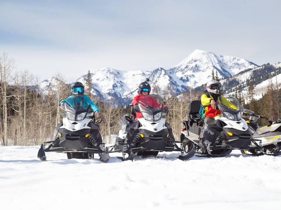 Three snowmobiles parked on a snowy surface with a mountainous background.