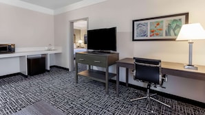 A hotel room with a desk, a television, a chair, a lamp, and a framed picture on the wall.
