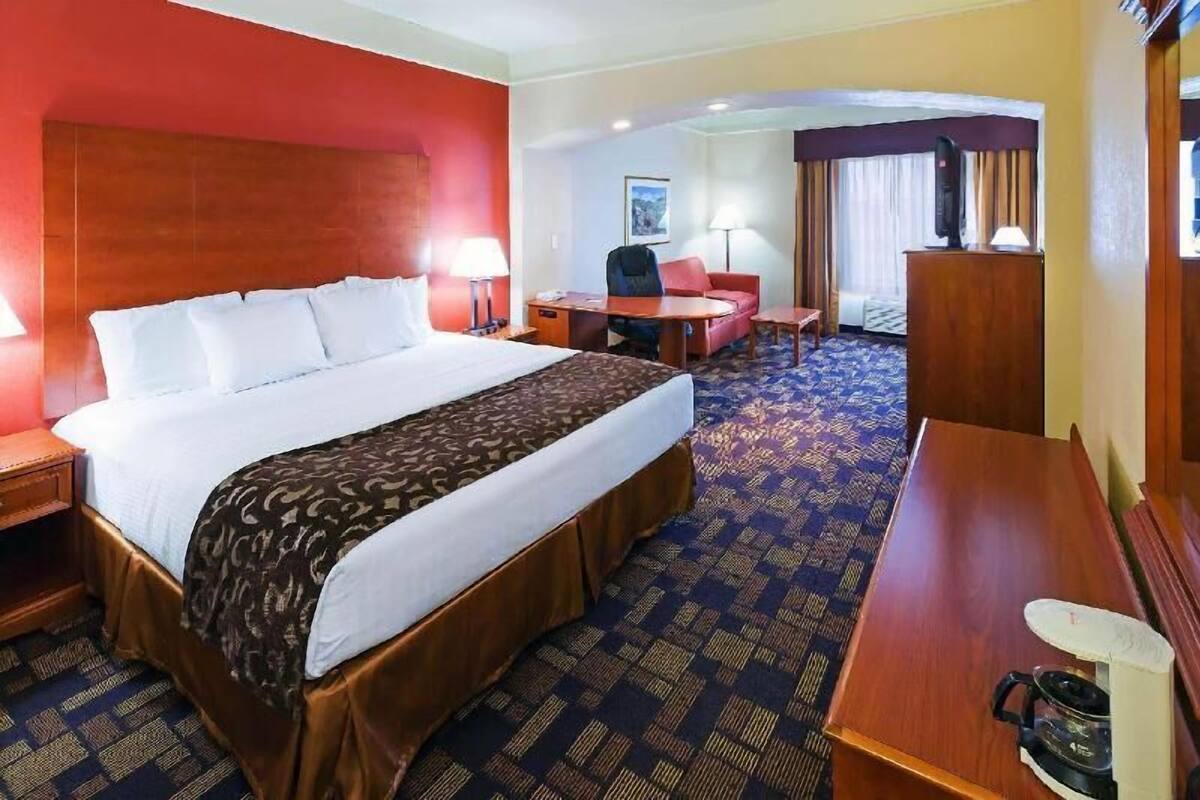 Une chambre d’hôtel avec un grand lit, un bureau, une chaise, une télévision et une fenêtre avec des rideaux.