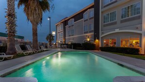 A swimming pool with lounge chairs, palm trees, and a hotel building with multiple floors and large windows.