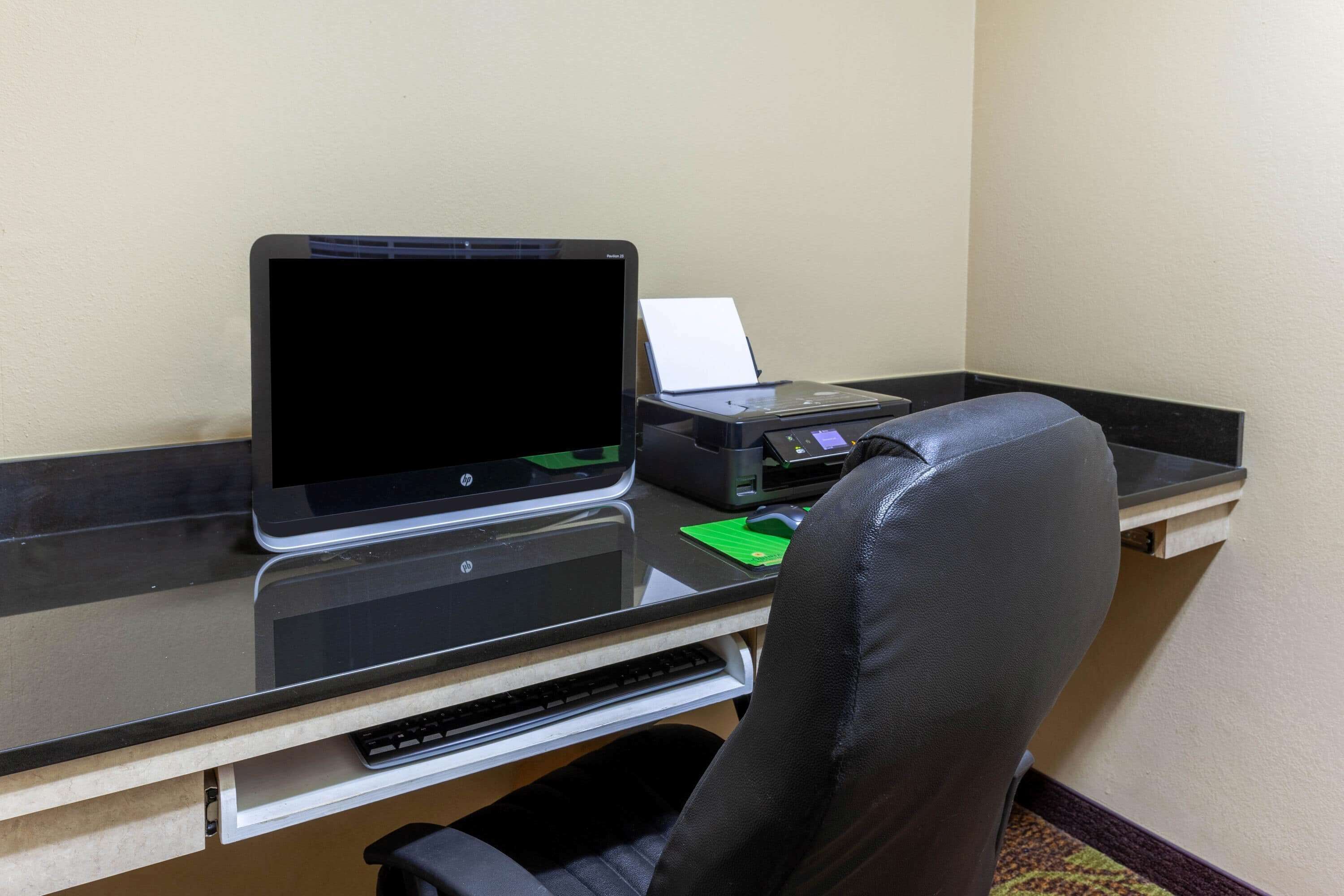 A hotel workspace with a laptop, printer, and a black leather chair.