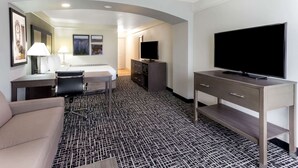 A hotel room with a bed, a desk with a chair, a TV, a sofa, and a patterned carpet.