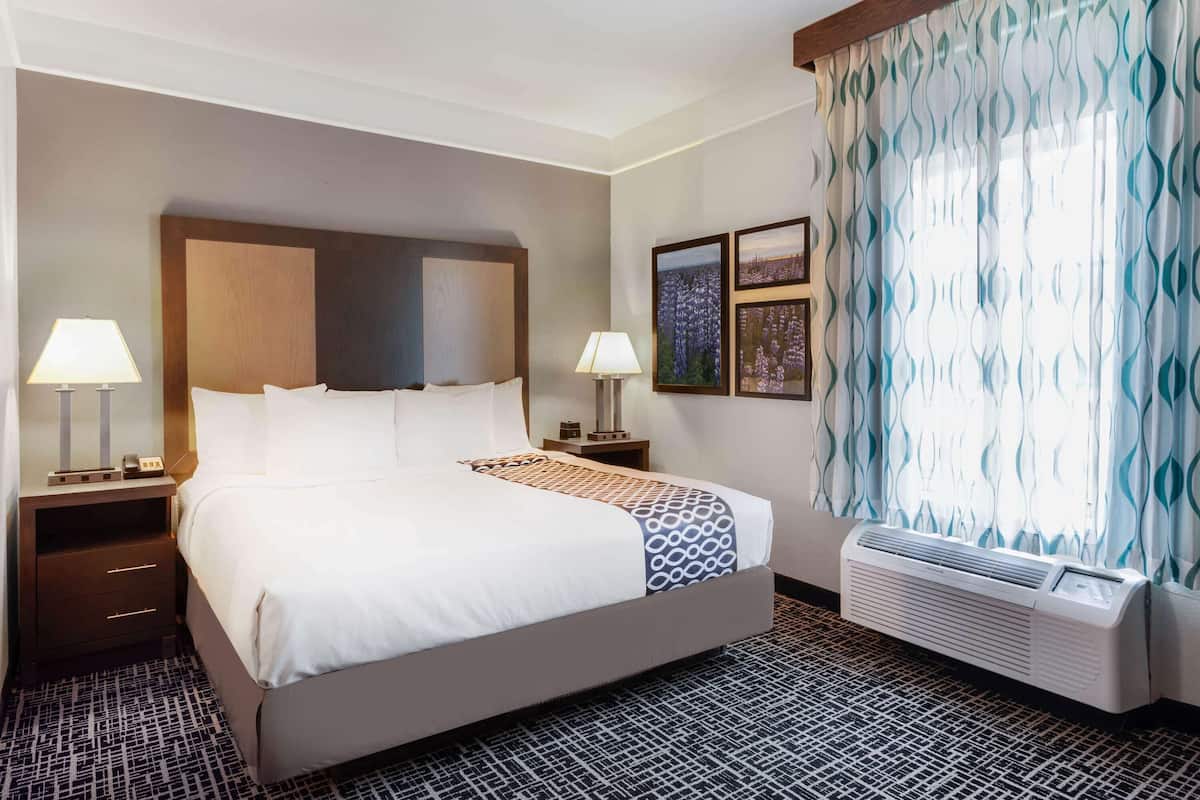 Une chambre d’hôtel avec un grand lit, deux tables de chevet avec des lampes, un climatiseur fixé au mur et des rideaux à motifs.