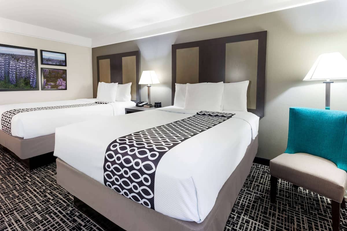 Une chambre d’hôtel avec deux lits, un bureau, une chaise et une lampe.