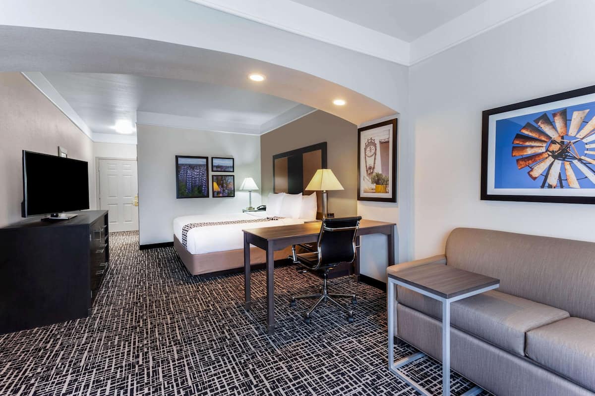 Une chambre d’hôtel équipée d’un lit, d’un bureau, d’une chaise, d’une télévision, d’un canapé et d’œuvres d’art accrochées aux murs.