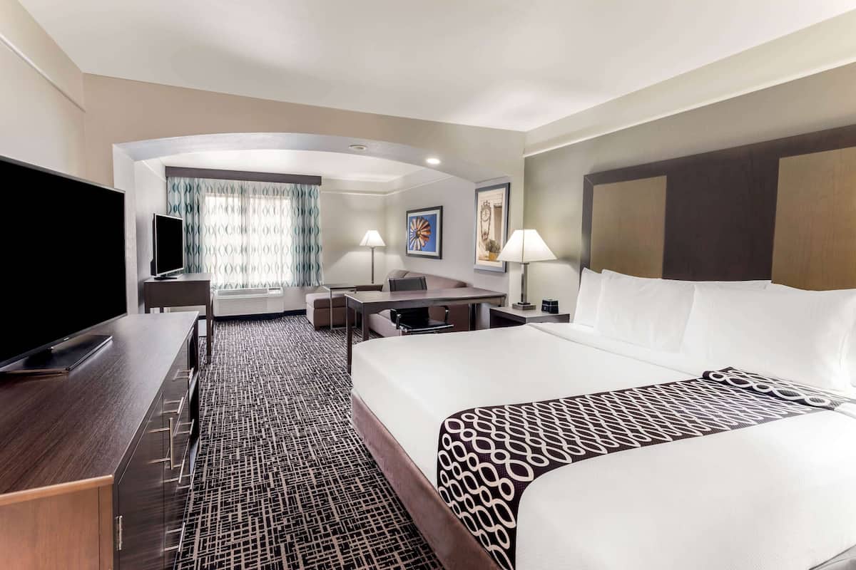 Une chambre d’hôtel dotée d’un grand lit, d’un bureau avec un téléviseur à écran plat, d’un coin salon avec un canapé et des fauteuils, et d’une grande fenêtre avec des rideaux.