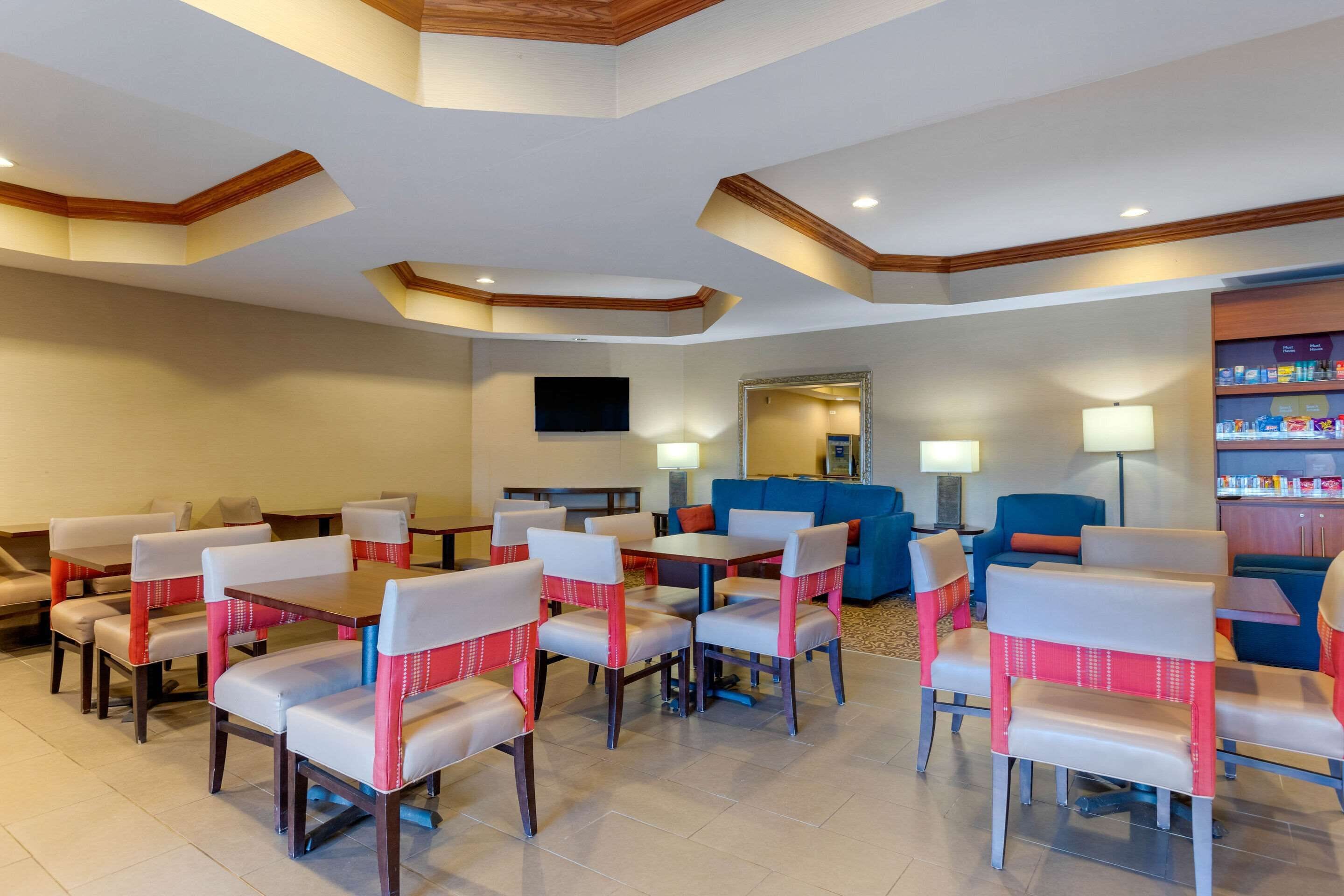 Un vestíbulo de hotel con varias mesas y sillas para comer, un sofá azul y un minibar.
