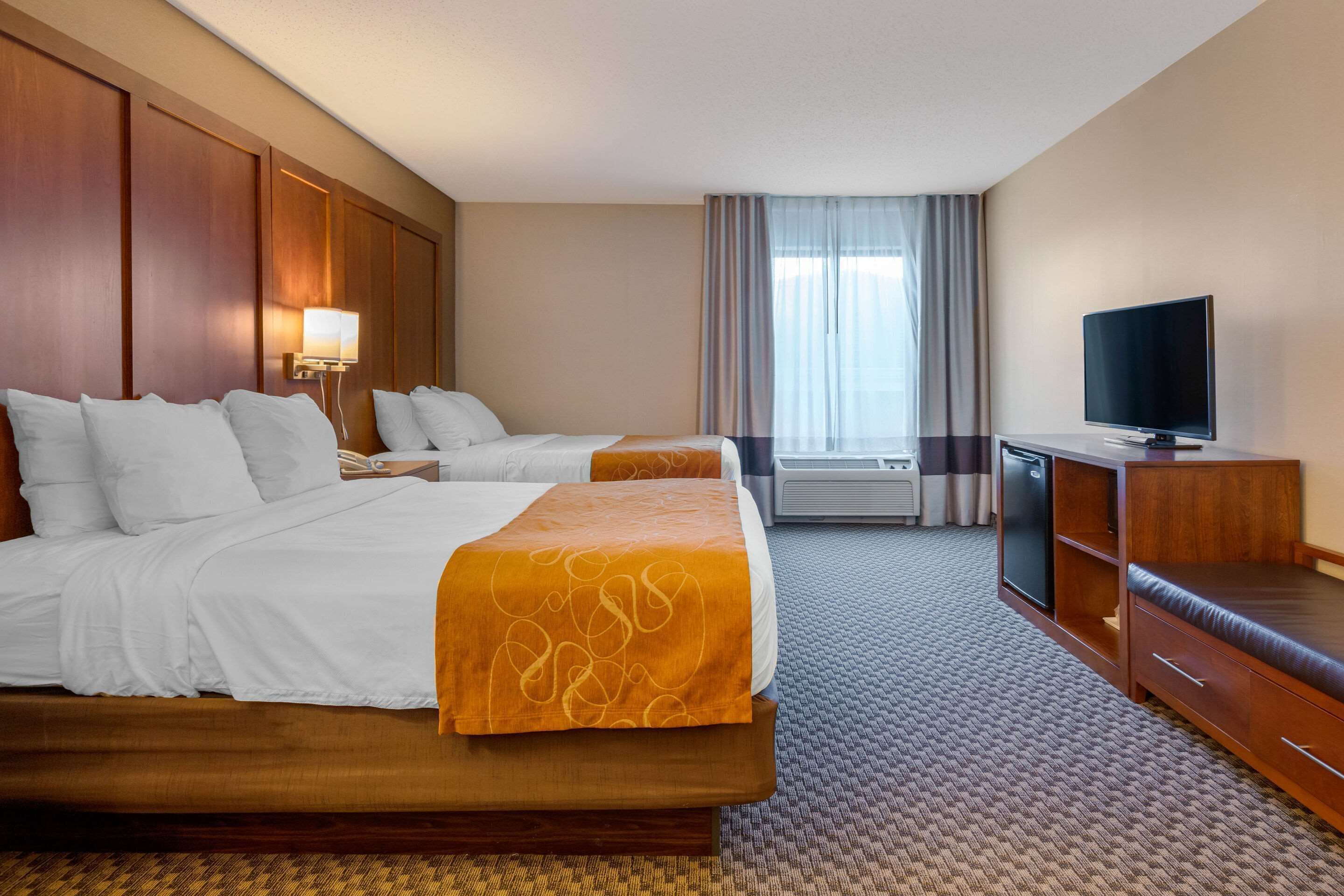 A hotel room with two beds, a television, a desk, and a window with curtains.
