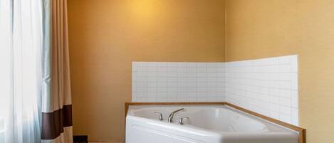 A bathroom with a bathtub, white tiled walls, and a wooden floor.