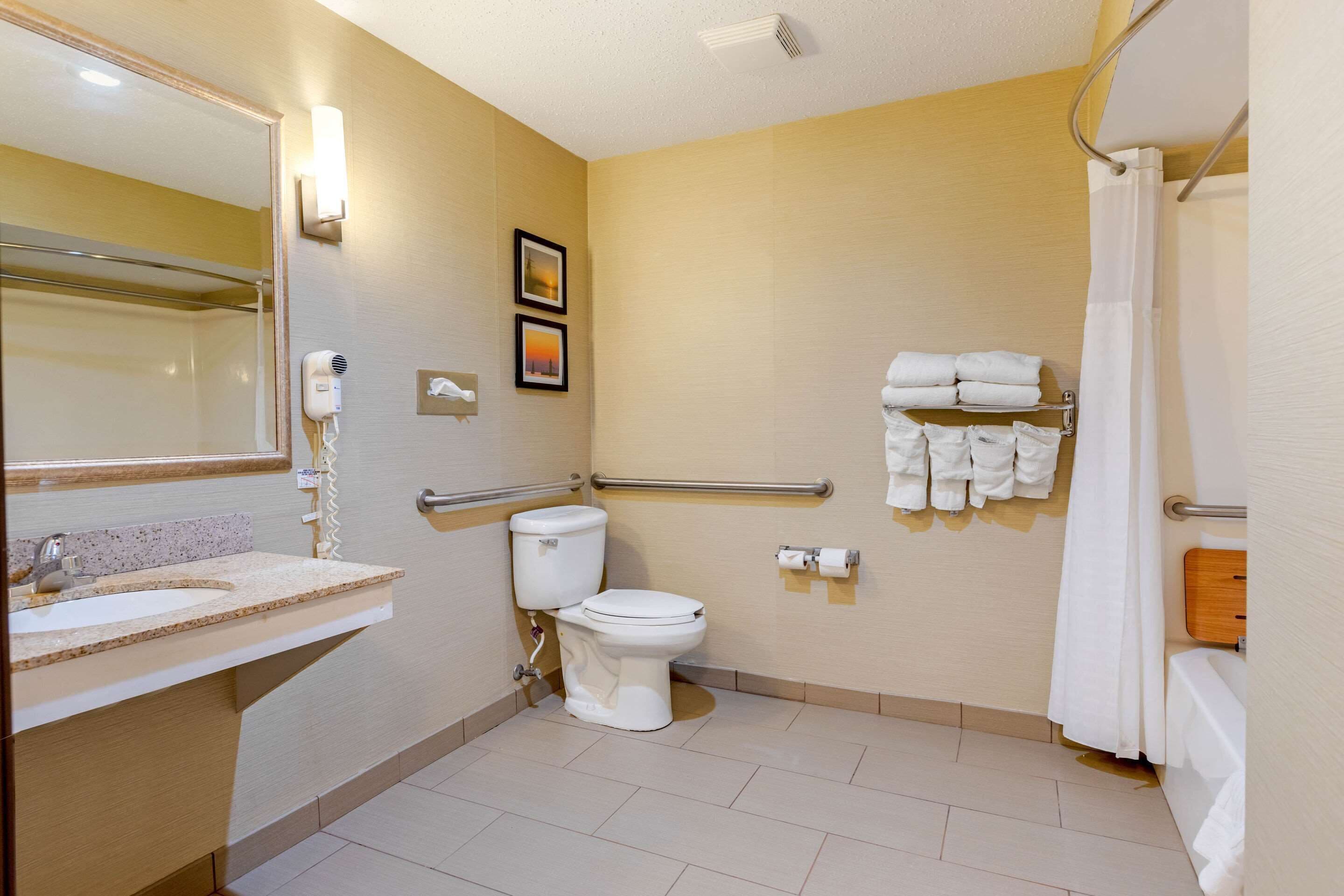 Une salle de bain équipée d’un lavabo, de toilettes et d’une douche. Des serviettes sont disposées sur un porte-serviettes et un sèche-mains est fixé au mur.